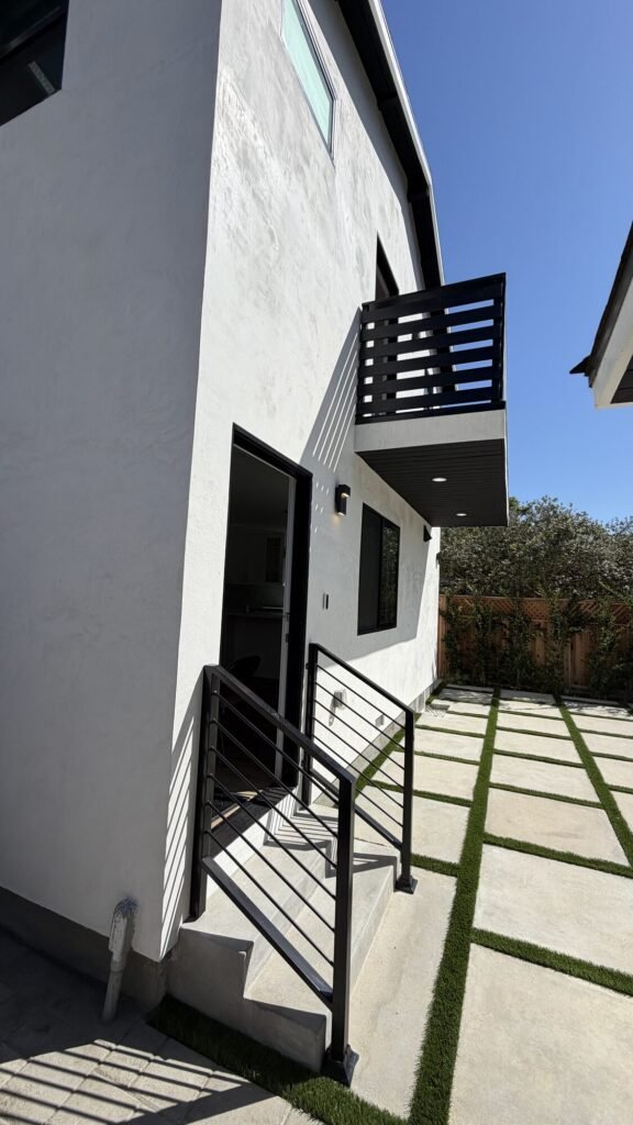 Modern two-story stucco addition with black balcony railing - Rafa Home Builders