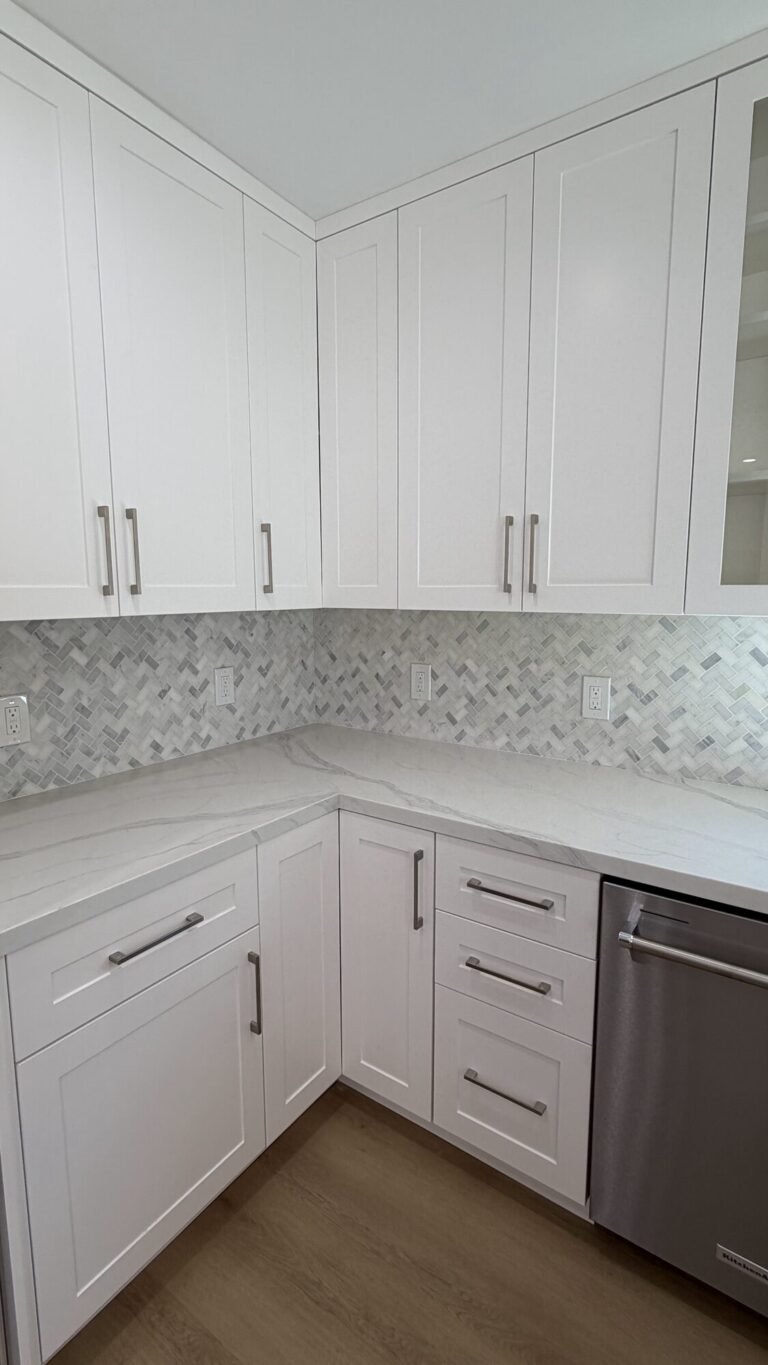 White shaker kitchen with quartz counters and a marble herringbone backsplash