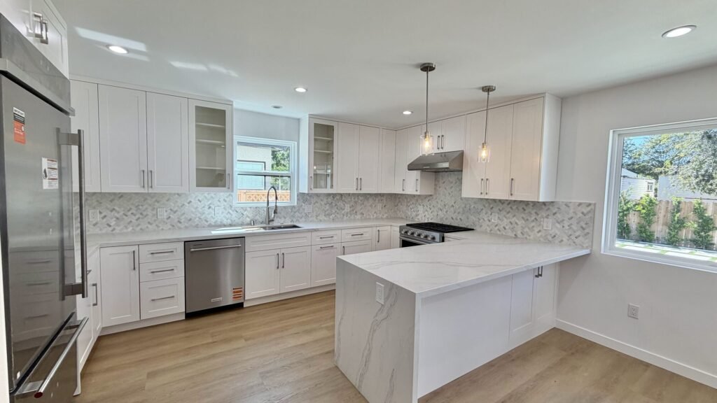 White kitchen remodel with quartz waterfall peninsula and stainless appliances - Rafa Home Builders